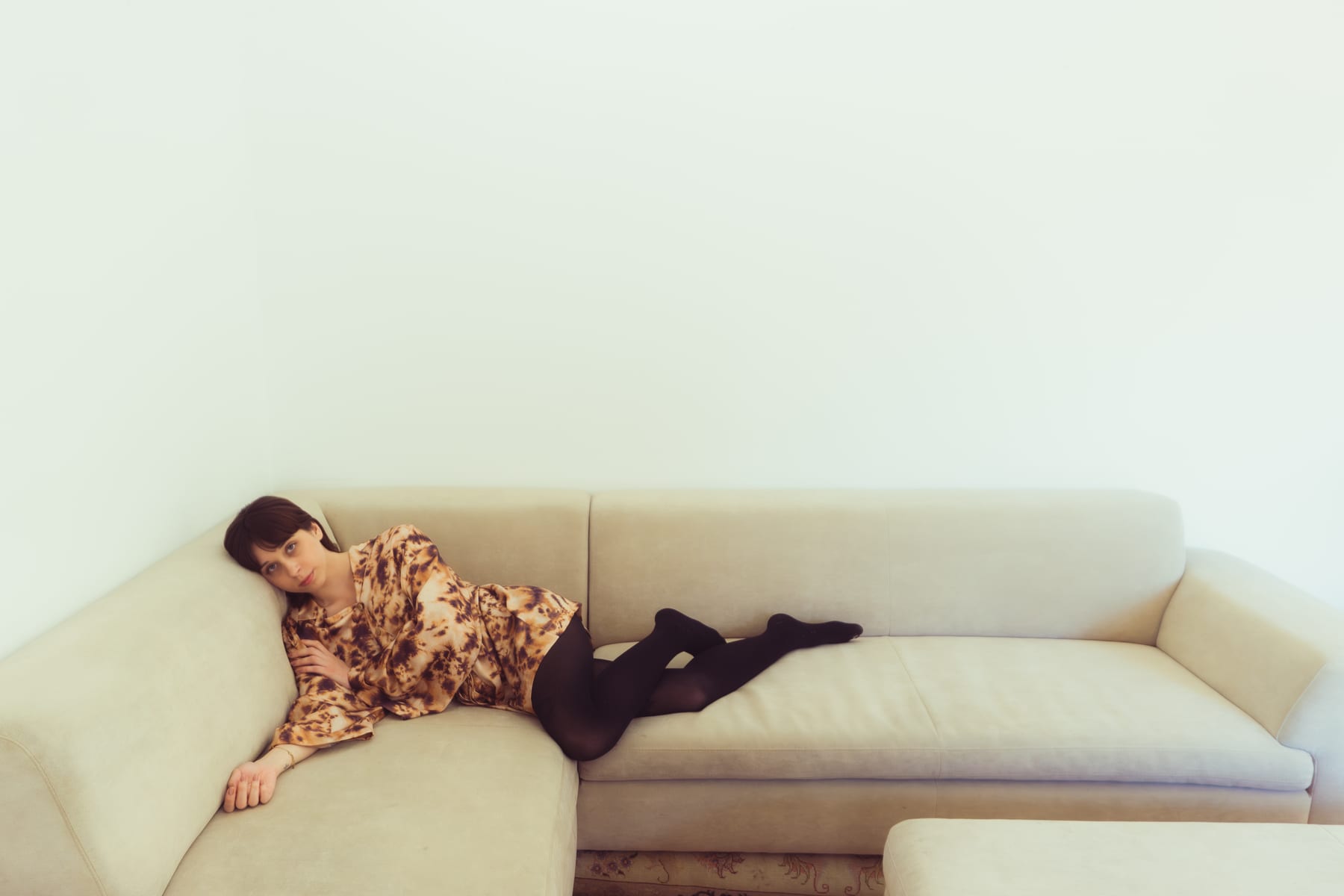 Model in an animal-print silk pyjama set lying along a long beige sofa in a bright room. (dummycopy)