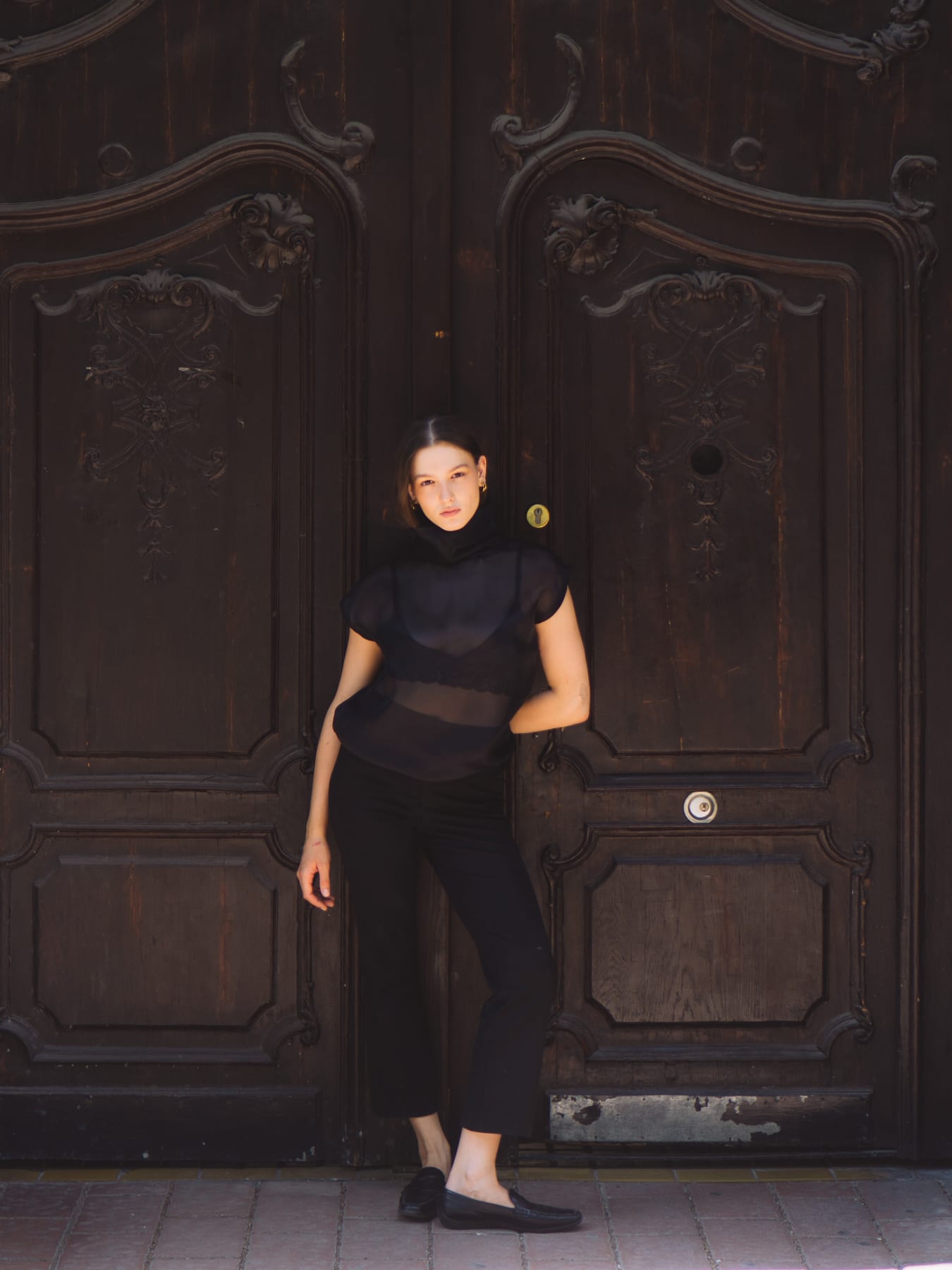 Model in black standing in front of a carved dark wooden gate.