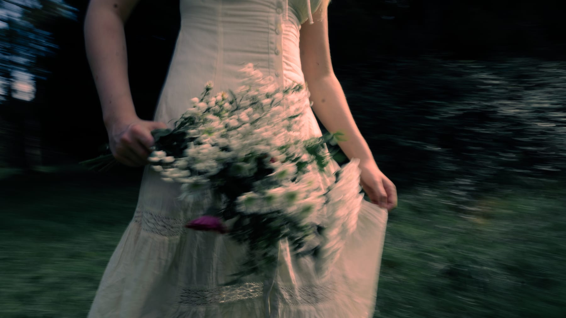 A pale dress and a bunch of wild flowers in motion, close up.