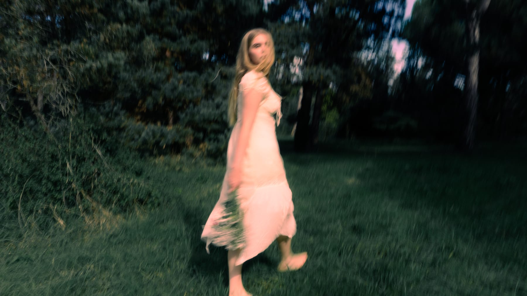 Woman in a pale dress walking through a meadow, looking back.