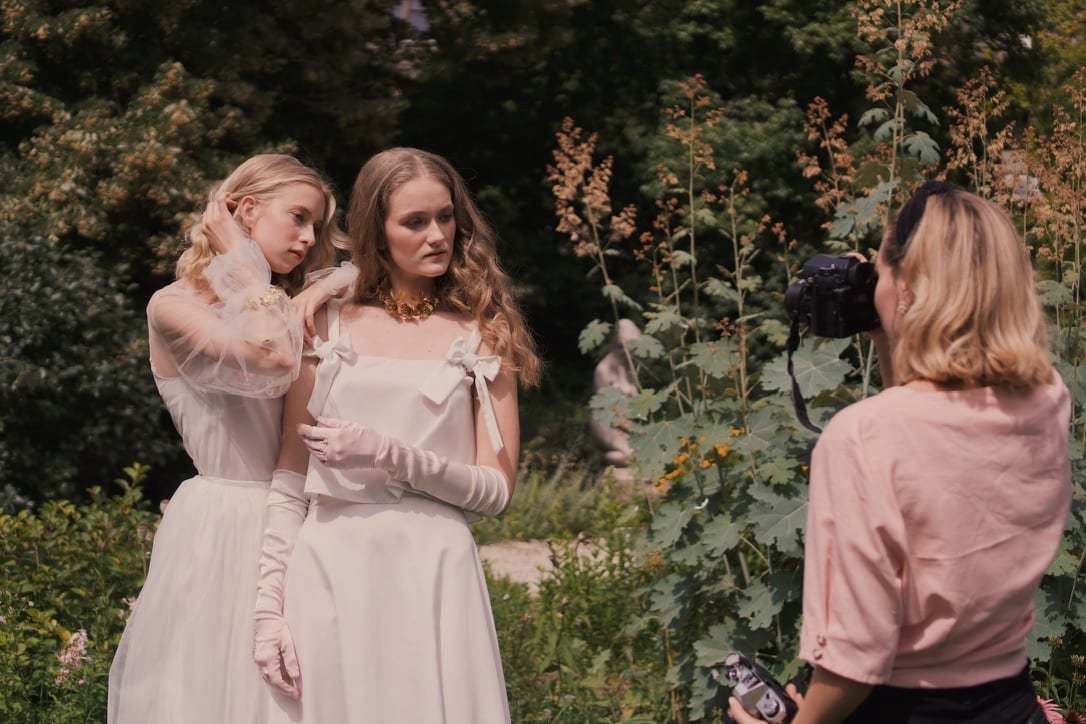 Two models in white and pale pink having their hair done outdoors, behind the scenes.