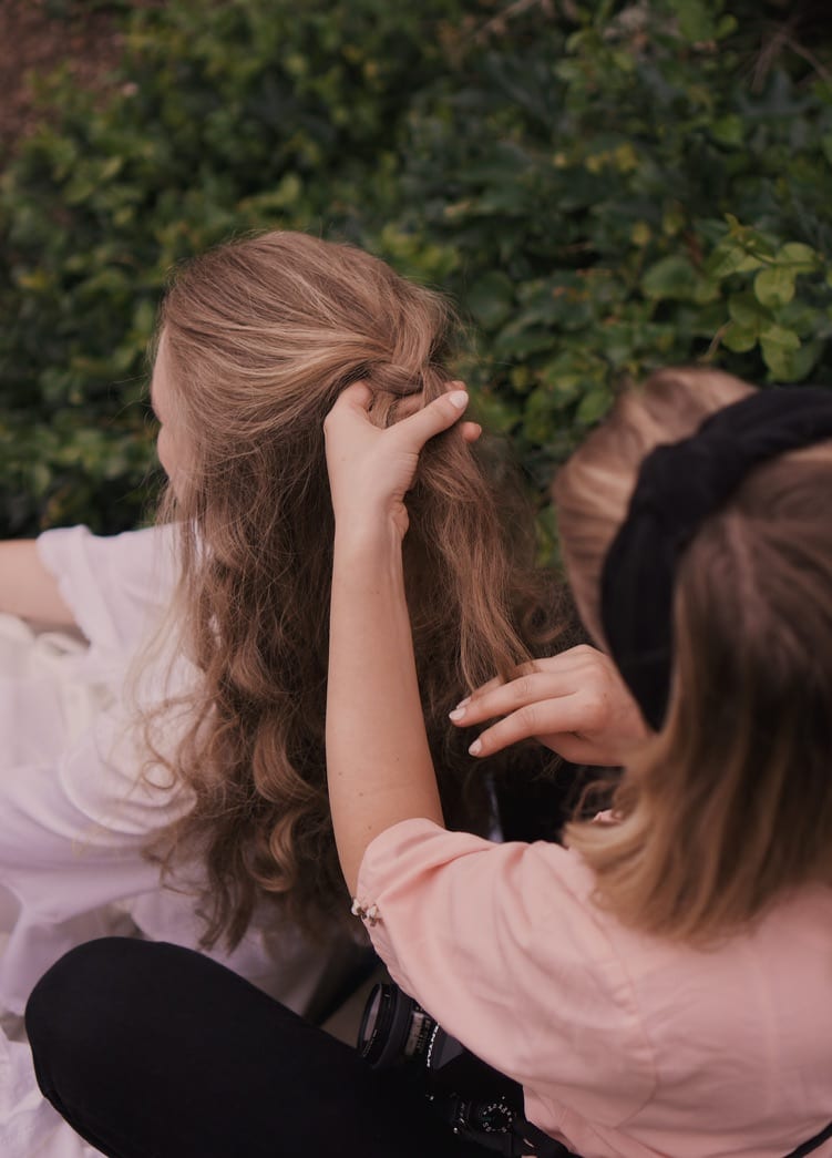 A stylist pinning up a model's blonde hair, close up, outdoors.