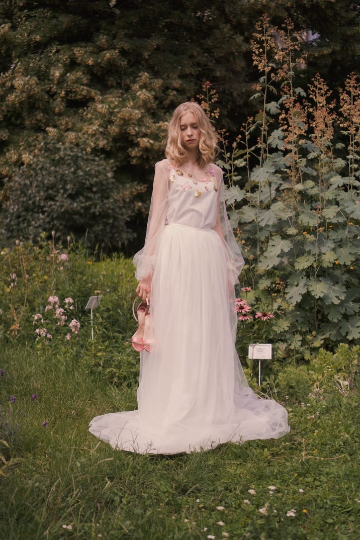 Model in a long white dress standing in a green garden.