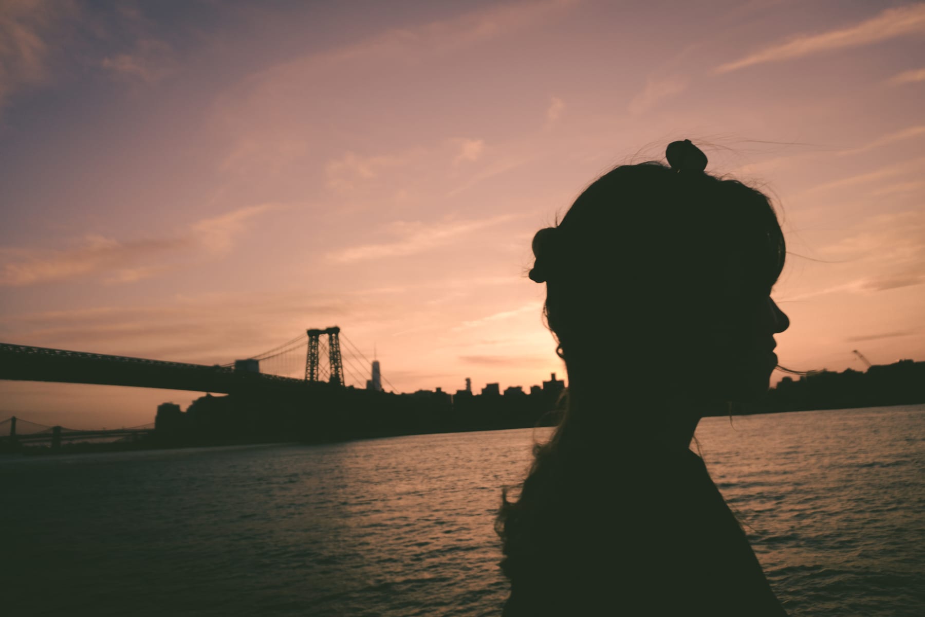 A silhouette in profile at sunset with the Williamsburg Bridge and the river behind. (dummycopy)